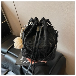 Detail of black drawstring bucket bag with textured fabric and plush puppy charm