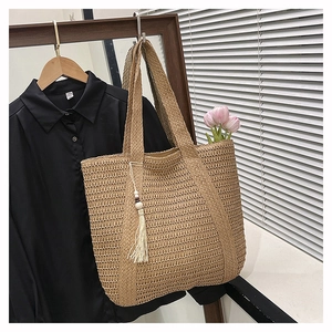 Detail of hand-woven straw tote bag with elegant white tassel and wooden bead accents