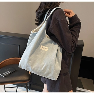 Detail of light blue denim tote bag with white bow embroidery and brand woven label