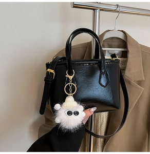 Détail du sac seau noir en cuir brillant avec charmant monstre en peluche blanc et bandoulière