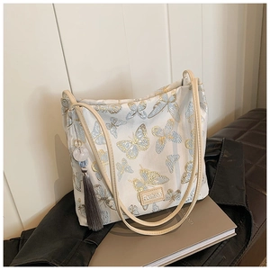 Detail of blue butterfly embroidery and tassel charm on beige canvas shoulder bag