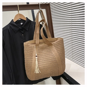 Detail of hand-woven straw tote bag with decorative white tassels and wooden beads