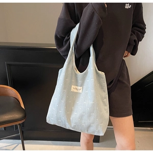 Detail view of light blue denim tote bag with white bow print and woven logo patch