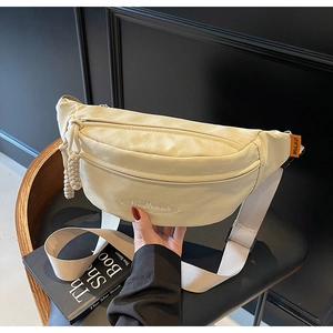 Detail of cream canvas belt bag showing embroidered logo and woven zipper puller