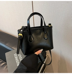 Détail d'un sac seau noir brillant avec garnitures dorées et logo embossé