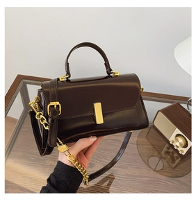 Close-up of deep brown glossy leather bag with gold buckle and chain strap detail