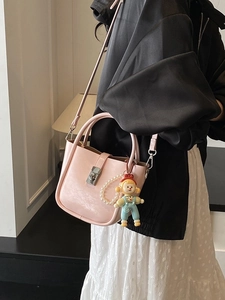 Pink PU bucket bag with pearl strap and cartoon doll charm shown on model in a soft room