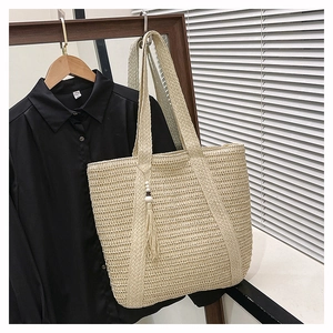 Detail of hand-woven straw tote bag featuring wooden beads and long tassel charm