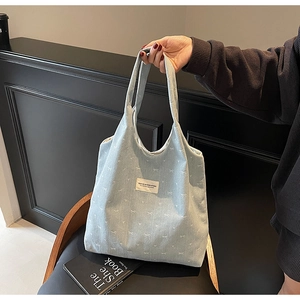 Detail of light blue corduroy tote bag with white bow prints and wide shoulder strap