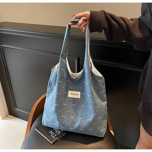 Detail of light blue denim tote bag with white bow patterns resting on a vintage chair