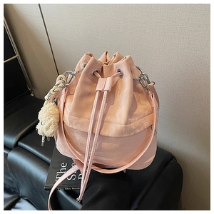 Detailed close-up of light pink drawstring bucket bag with plush charm and long strap
