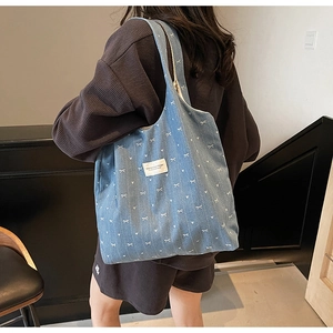 Detail shot of blue denim tote bag featuring white bow and heart prints on shoulder