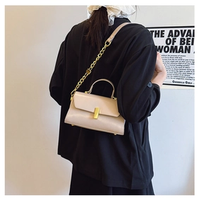 Detail view of beige square bag with golden buckle, chain strap, and bottom studs