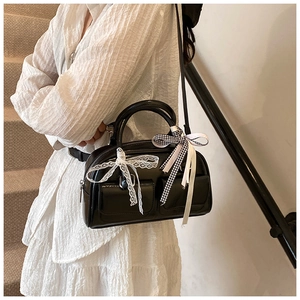 Detail of black glossy bowling bag featuring white lace bow and checkered ribbon strap