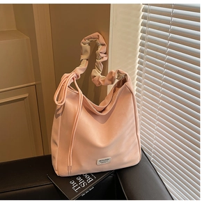 Detail of a pink leather tote bag featuring a stylish ruched handle and metal logo plaque