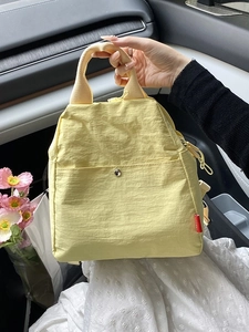 Light yellow lightweight nylon crossbody bag with metal buckle and top handle in car setting