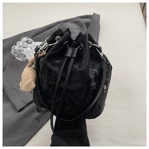 Detail of black drawstring bucket bag with pleated texture and cute plush pendant charm