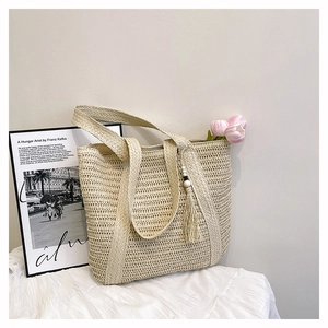 Detail of beige straw woven tote bag featuring hollow mesh texture and tassel with wooden beads