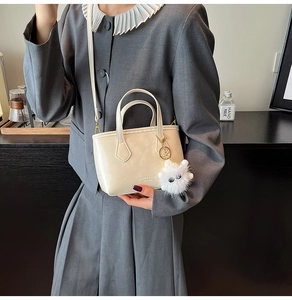 Creamy white crossbody bucket bag with fuzzy monster charm and fashion leather text detail