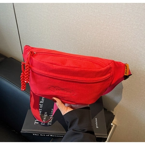 Close-up of a red canvas fanny pack with logo embroidery and zip closure on books