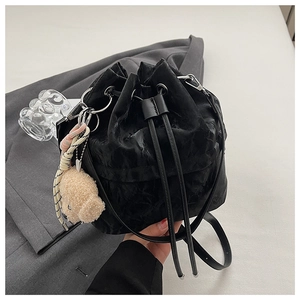 Detail of black drawstring bucket bag with pleated leather texture and plush puppy charm