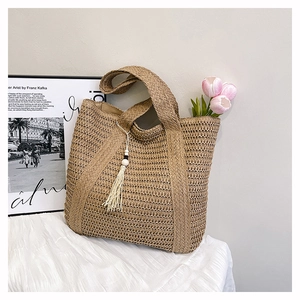 Detail view of woven straw tote bag featuring decorative white tassels and beads