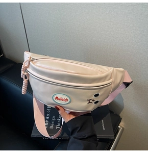 Dettaglio borsa beige con ricamo a orsetto e tracolla in nylon rosa appoggiata su libri