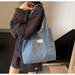 Detail of blue denim tote bag with white bow prints on a model in a stairwell