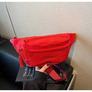 Detail of red canvas waist bag with braided zipper pull and orange brand tag on side