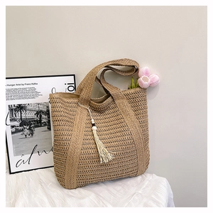 Detail of hand-woven straw tote bag with decorative white tassels and wooden beads