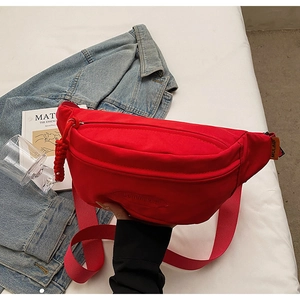 Detail of red canvas crossbody chest bag showing adjustable strap and brand woven label