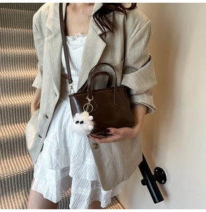 Détail du sac seau marron avec logo doré et charm de sac en peluche blanche mignonne