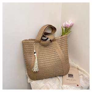 Detail of hand-woven straw tote bag with elegant tassel charm and natural texture
