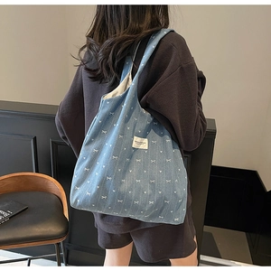 Back view of a light blue denim tote bag with white bow patterns worn by a model