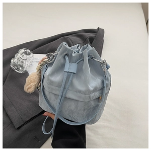 Close-up of light blue pleated bucket bag with drawstring closure and plush pompom charm