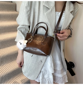Détail d'un sac seau en cuir marron foncé avec pendentif en peluche et logo texte