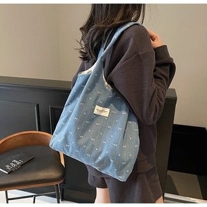 Detail of blue denim tote bag featuring white bow prints and a logo patch on the side