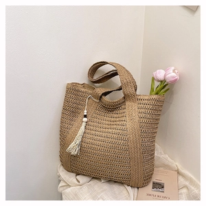 Close-up of handmade straw tote bag with white cotton tassels and wooden beads detail