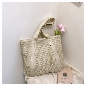 Detail of beige straw tote bag with beaded tassel and woven texture on a white background