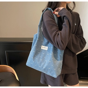 Close-up of denim tote bag featuring white bow heart prints and a woven brand label
