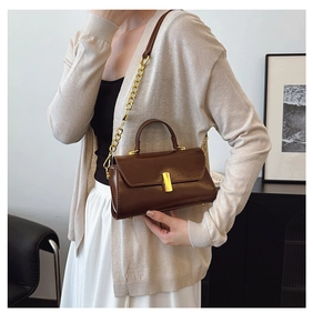 Detail of a brown leather crossbody bag with a gold metal clasp and chain strap
