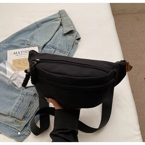 Detail of black canvas chest bag featuring orange MULADI label and cord zipper puller