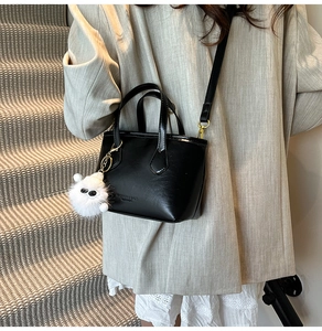 Détail d'un sac seau noir avec charme en peluche porté par un mannequin en intérieur