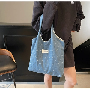 Detail of blue denim tote bag with white bow embroidery and branded label on model