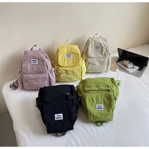 Flat lay of multiple color canvas backpacks with laptop and books on a white bed