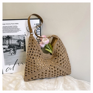 Detail of hollow crochet pattern on khaki straw tote with brown leather handle