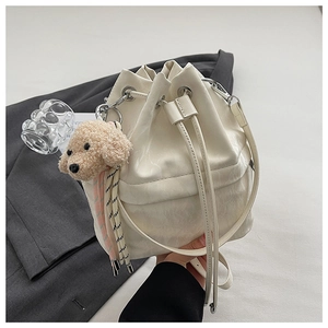 Detailed side view of white drawstring bucket bag with plush dog charm and silver hardware