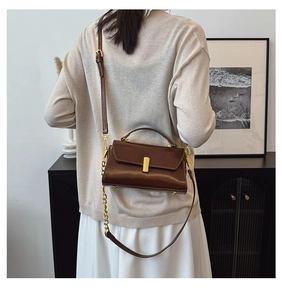 Detail of dark brown leather handbag with gold buckle shown on a model in home setting