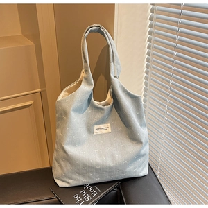 Close-up of light blue denim tote bag with white bow patterns and fabric studio label