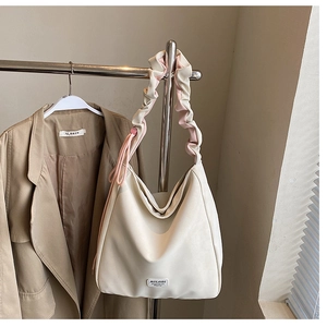 Detail of a large cream hobo bag with ruched strap and brand logo patch for daily commute